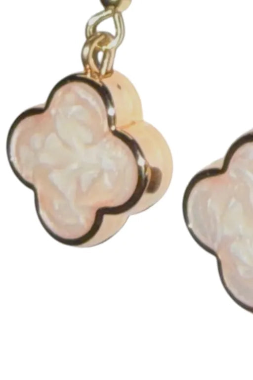 Pair of earrings with gold frames and pinkish-white clover-shaped centers on a white background.